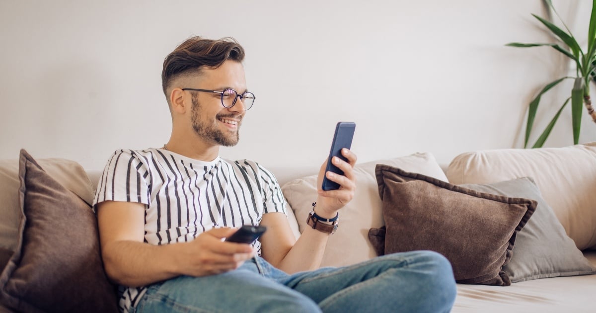 man using tv remote and cell phone